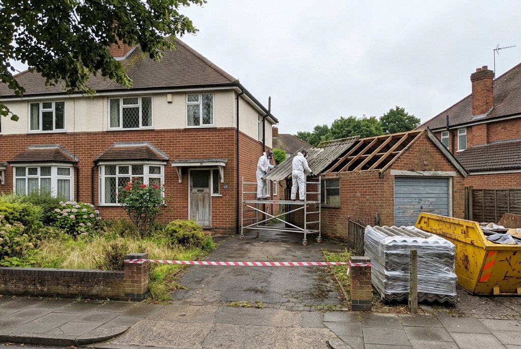 Garage roof removal in progress with waste skip and cordon